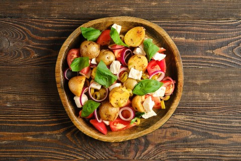 Top view of bowl with warm salad made with potato, feta cheese, tomatoes, onions, and basil. Salad