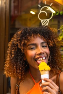 Happy young black woman with curly hair enjoying a refreshing yellow ice cream cone on a sunny day,