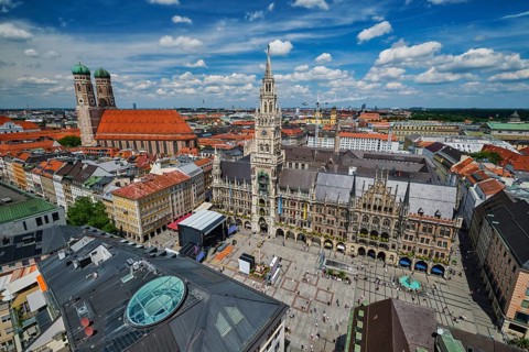 Wide high-angle view of the bustling Marienplatz square, the New Town Hall, and Frauenkirche under