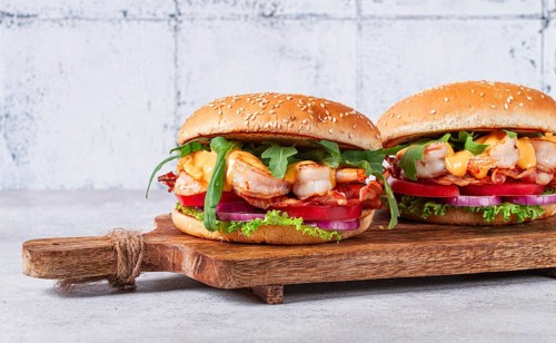 Two shrimp burgers and buns with sesame seeds, bacon, lettuce, tomatoes and onions, On a wooden