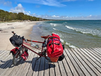 A loaded bike stands on a wooden floor near the coast with blue sky and waves, bicycle trip,