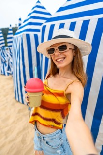 Woman wearing a straw hat and stylish sunglasses smiling happily while holding an ice cream shaped