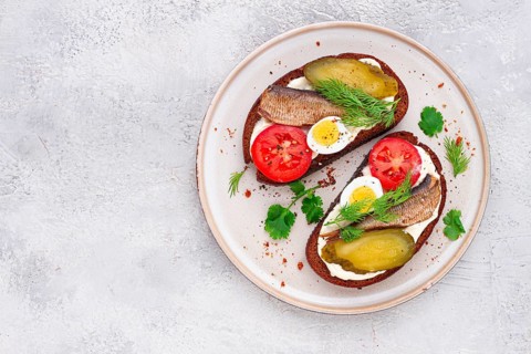 Sandwiches on rye bread, with sprats, quail eggs, fresh tomatoes and pickled cucumber, appetizer,
