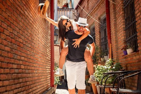 Happy interracial couple having fun piggyback ride in Tbilisi old city narrow street.Cheerful young