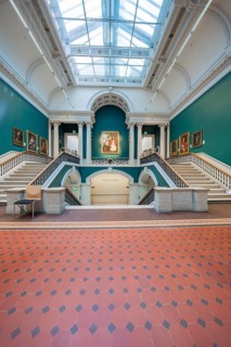 Entrance area of an art gallery with stairs and green walls decorated with paintings, National
