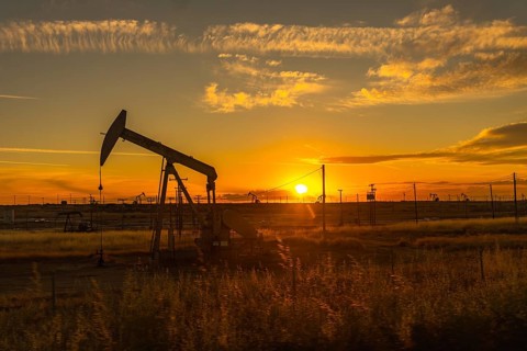Pumpjack extracting crude oil from a well in a large oil field, silhouetted against a vibrant