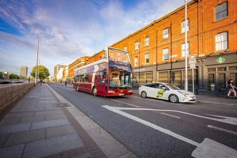 A double-decker bus and a car ride on a road next to red brick buildings, Dublin, Ireland