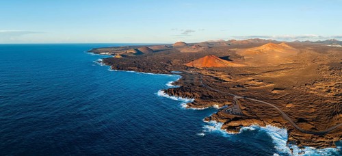 Coast with lava fields, volcanic landscape near Los Hervideros with red volcano Montaña Bermeja, in