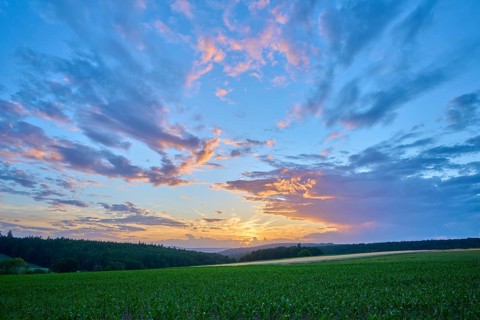 Sunset over a green field with dramatic clouds and intense sky, summer, Großheubach, Miltenberg,