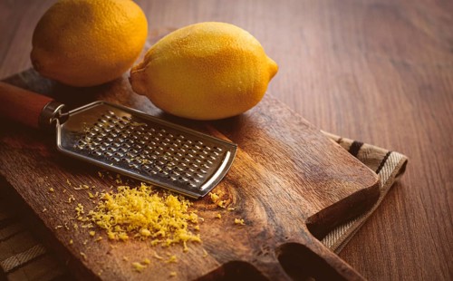 Lemons and grated orange peel, with a zest grater, on a chopping board, close-up, no people