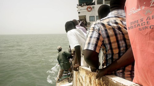 People look at a small boat from the deck of a rusty ferry a boat trip, Bubaque, Bijagos
