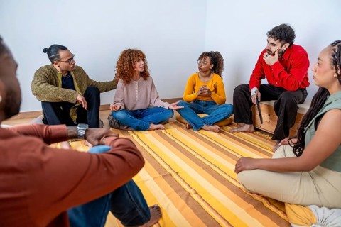 Diverse adults seated in a circle indoors, sharing stories and actively listening in a supportive