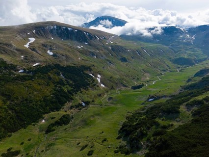 Extensive mountain landscape with green meadows and scattered clouds in the sky, aerial view, near