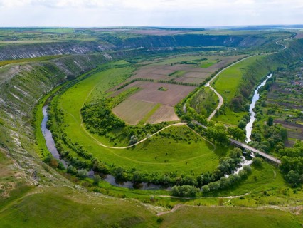 Wide, panoramic view of a river running through green fields and hills, aerial view, loops of the