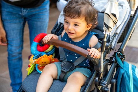 Smiling toddler sitting securely in a modern stroller, holding onto the safety bar and observing