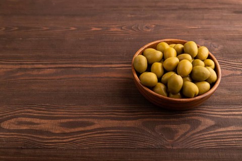 Fresh green olives in wooden bowl on brown wooden background. side view, copy space