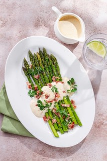 Fresh asparagus with cream sauce and bacon, on a white oval plate, light marble table, sunlight,