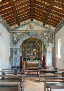 Historic interior of San Rocco Church with religious frescoes, stone arch, altar, wooden pews, and