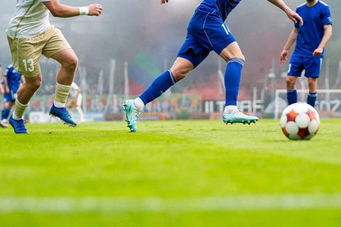 Close-up of soccer players in blue and white uniforms running toward ball on green field, real