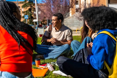 Diverse group of college students sitting on grass at a university campus, chatting, studying and