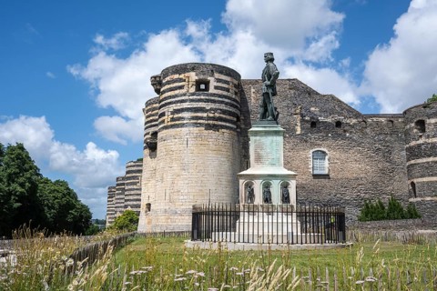 Bronze statue of King René on a decorated stone base in the foreground in front of one of the