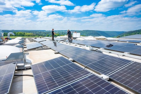 Two workers look after solar cells on a large roof under a blue sky, PV Montage, Perrot, Calw,