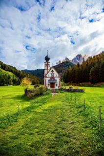 Church in a vast green valley surrounded by mountains and forests with blue skies and clouds,