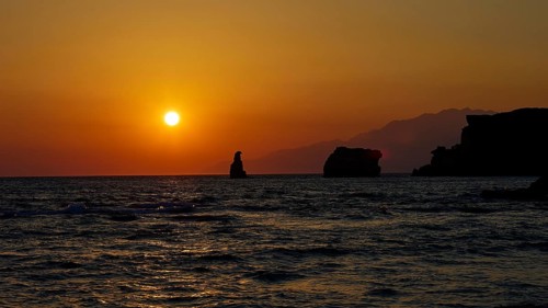 Calm sunset over the sea with mountains in the background and a rock in the water, sunset, south of