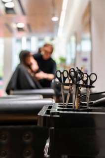 Professional hair cutting scissors standing in a black barber cart as a blurred hairdresser styles