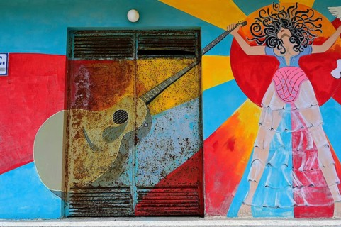 Colourful mural with a guitar and a stylized female figure at a door, Matala, Neolithic caves,