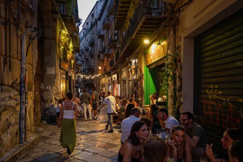 Busy narrow street with mostly young people dining outside restaurants, atmospheric lighting,