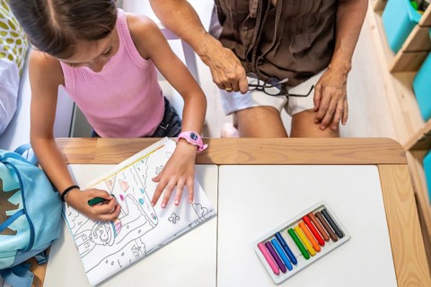 Grandmother and granddaughter bonding, coloring a book at a desk with crayons, enjoying creative