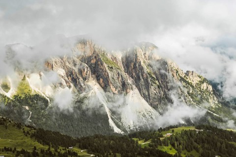 Dramatic limestone cliffs rock formations scree slopes dense alpine pine forest low clouds mist