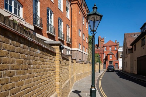 London taxi drives through narrow street lined with historic brick buildings, a street lamp and a