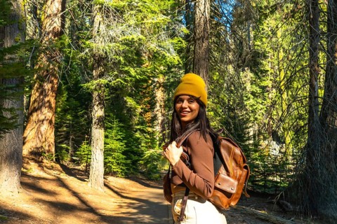 Young woman smiling and looking at camera, wearing a yellow beanie and backpack, enjoying her