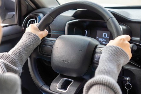 Detail of student driver's hands gripping steering wheel, digital speedometer showing zero, airbag