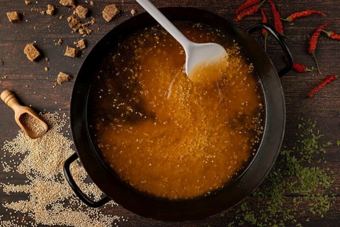 Quinoa is stirred in a pan with broth, surrounded by spices and hot peppers