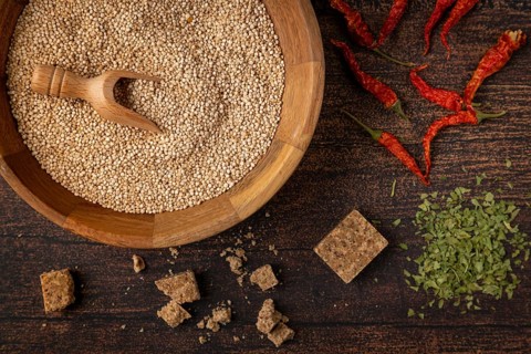 A bowl filled with quinoa next to spices and dried red peppers on a wooden table