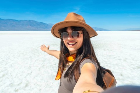 Young woman traveler smiling and extending arm, capturing a vibrant selfie on the vast salt flats