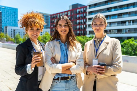 Executive women standing outdoors in an urban setting, smiling and holding coffee cups, symbolizing