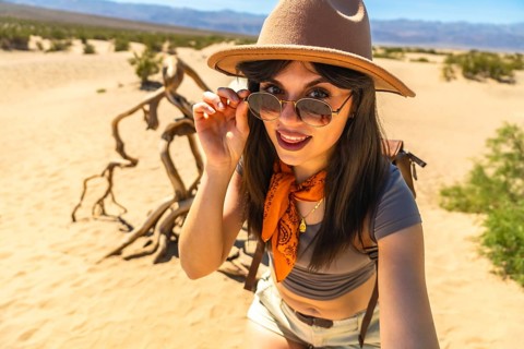 Young woman smiling, lifting sunglasses, and capturing a close up selfie while exploring the vast