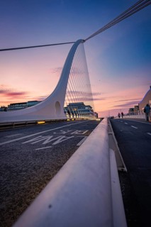 Futuristic bridge at sunset with purple and blue sky, city in background, Samuel Beckett Brg,