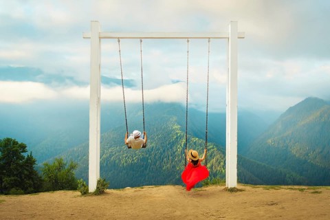 Couple riding giant swing above mountain valley with forest, clouds and panoramic landscape,