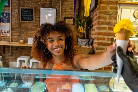 Happy young woman with curly hair smiling as she serves a refreshing scoop of yellow gelato in a