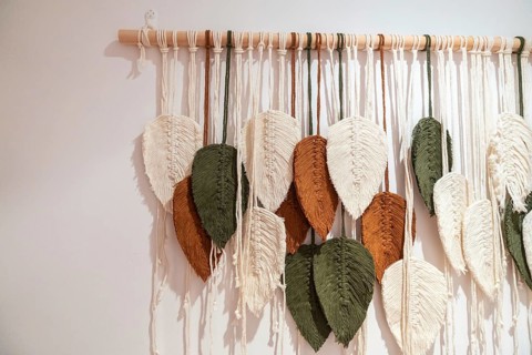 Macrame wall hanging featuring handcrafted leaf shapes in natural tones of cream, olive green, and