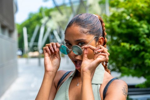 Young woman lowering round sunglasses, showing a wide open mouth expression of shock or surprise