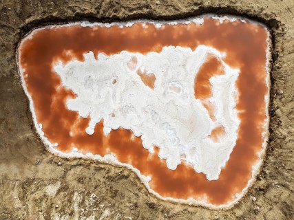 Saline pond with ruddy algae growth and white salt deposits at the Skeleton Coast. Aerial view.