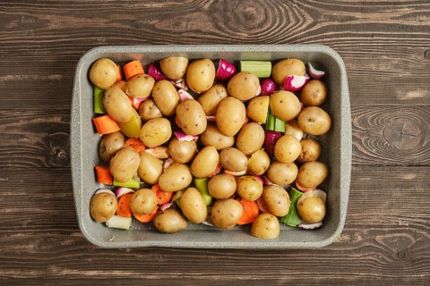 A baking dish holds an assortment of baby potatoes and chopped vegetables like carrots and celery.