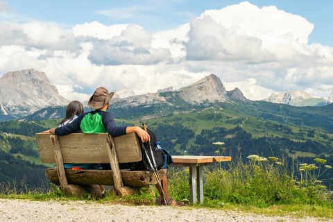 Caucasian couple hikers sit on hand made wooden bench, admiring the majestic Dolomites mountain