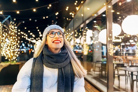 Happy young woman in winter attire under festive evening lights. A woman wearing a gray knit hat,